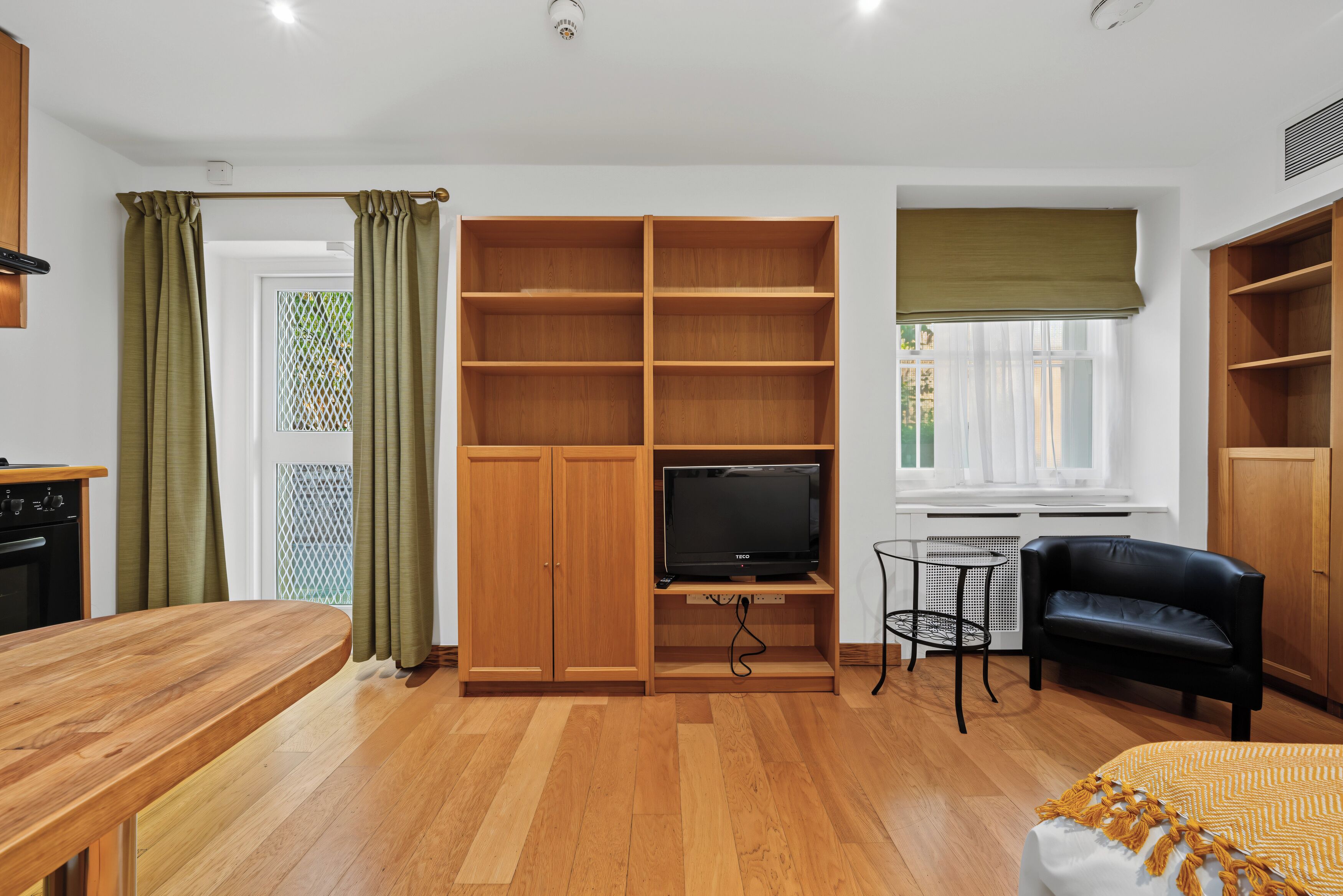 A compact living space with a wooden entertainment unit, a television, a dining area, and a seating area with a black sofa.