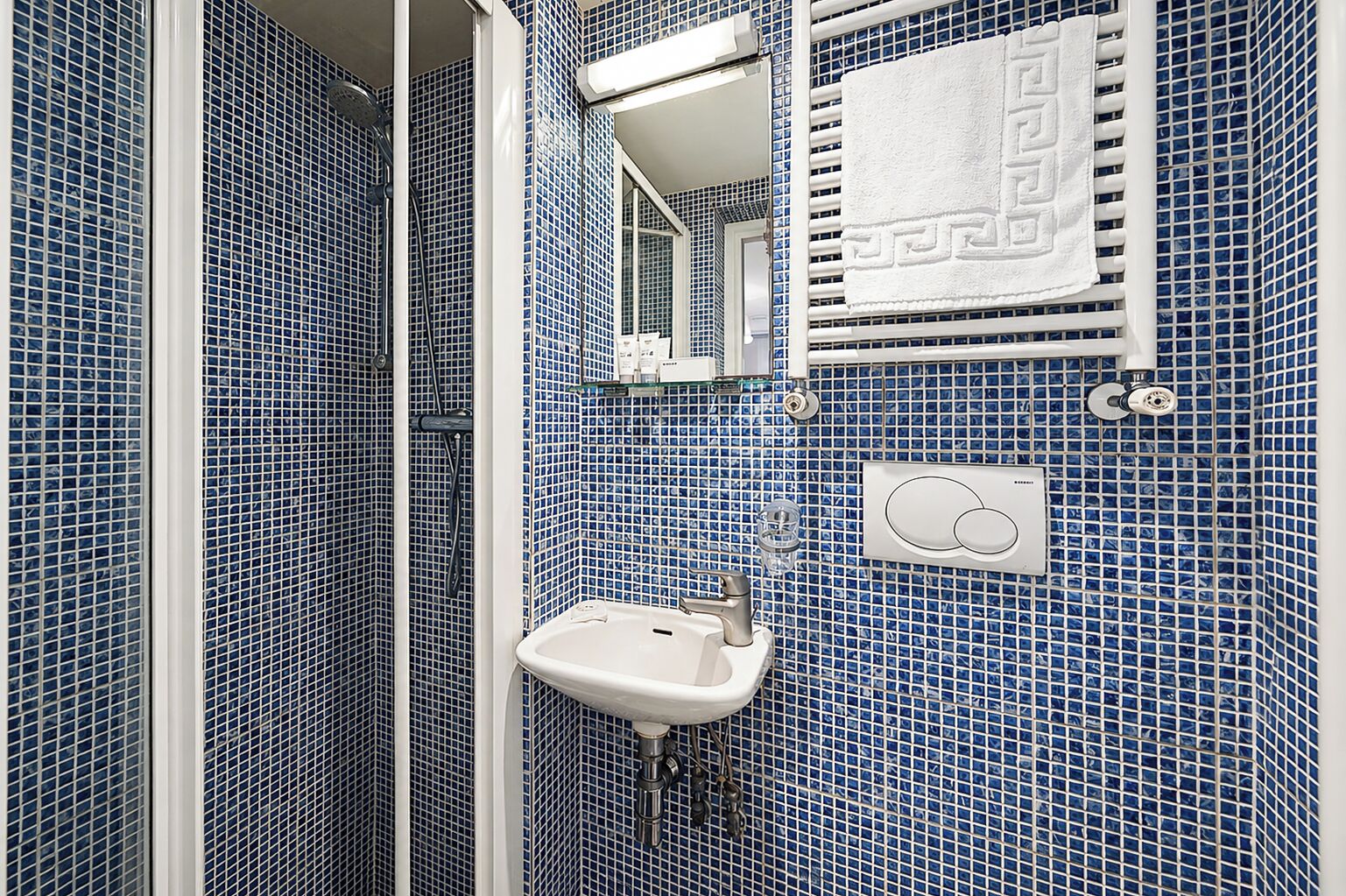 Un bagno con piastrelle a mosaico blu, un lavandino bianco, un portasciuga e uno specchio.