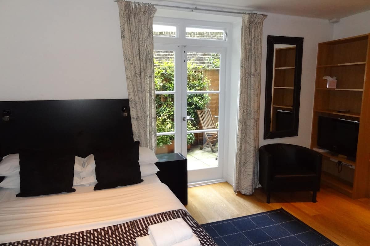 A hotel room with a large bed, a TV, a small desk, a chair, and a view of a garden through a glass door.