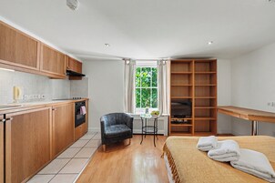 Una cucina compatta con mobili in legno, un'area pranzo con tavolo e sedie, un letto con coperta e una finestra vista su spazi verdi.