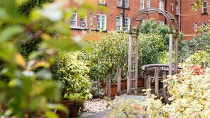 A garden with a wooden archway, potted plants, and a brick building in the background.