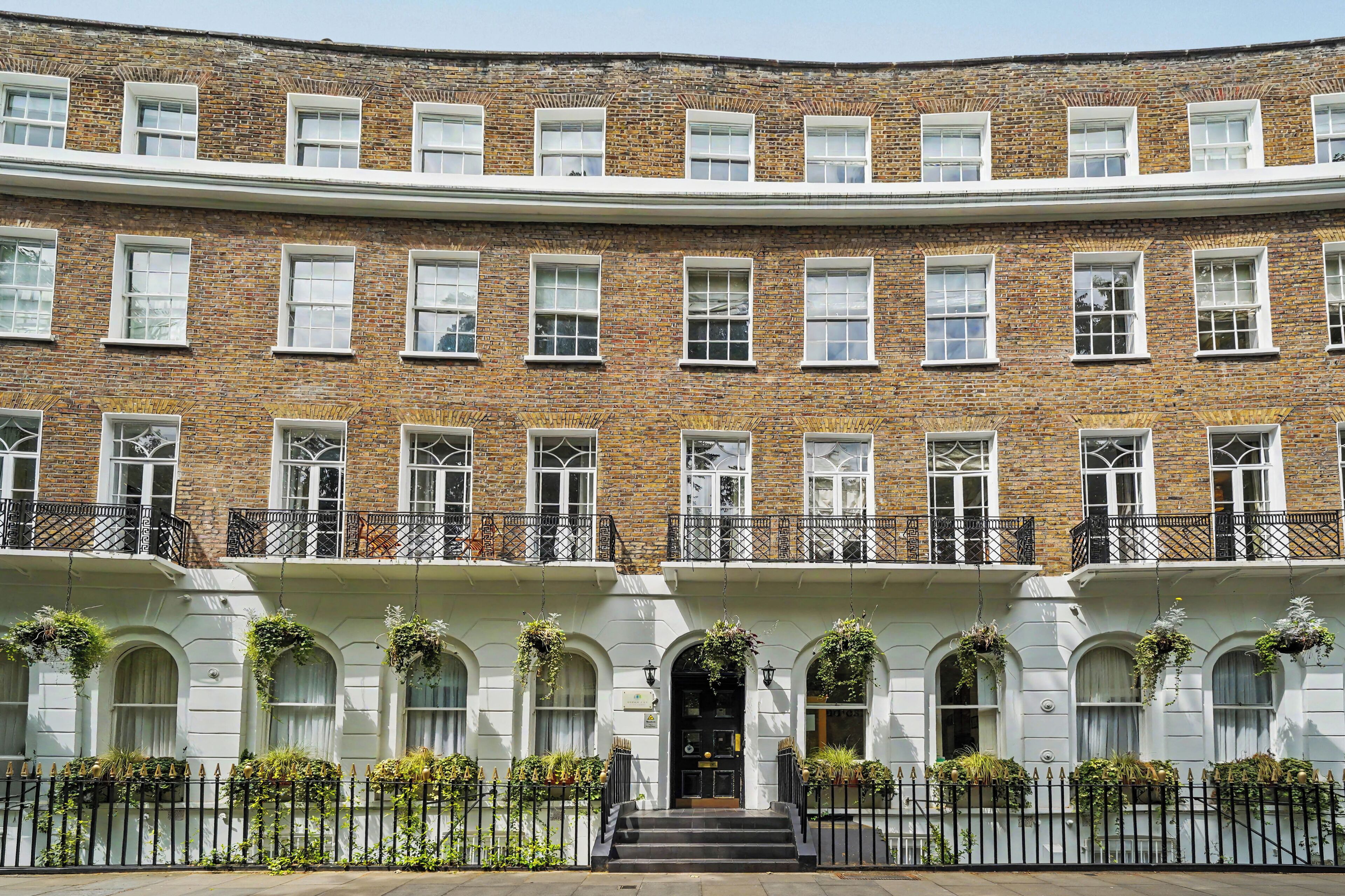 A multi-story building with a brick facade, white-framed windows, and a black metal fence with hanging planters.