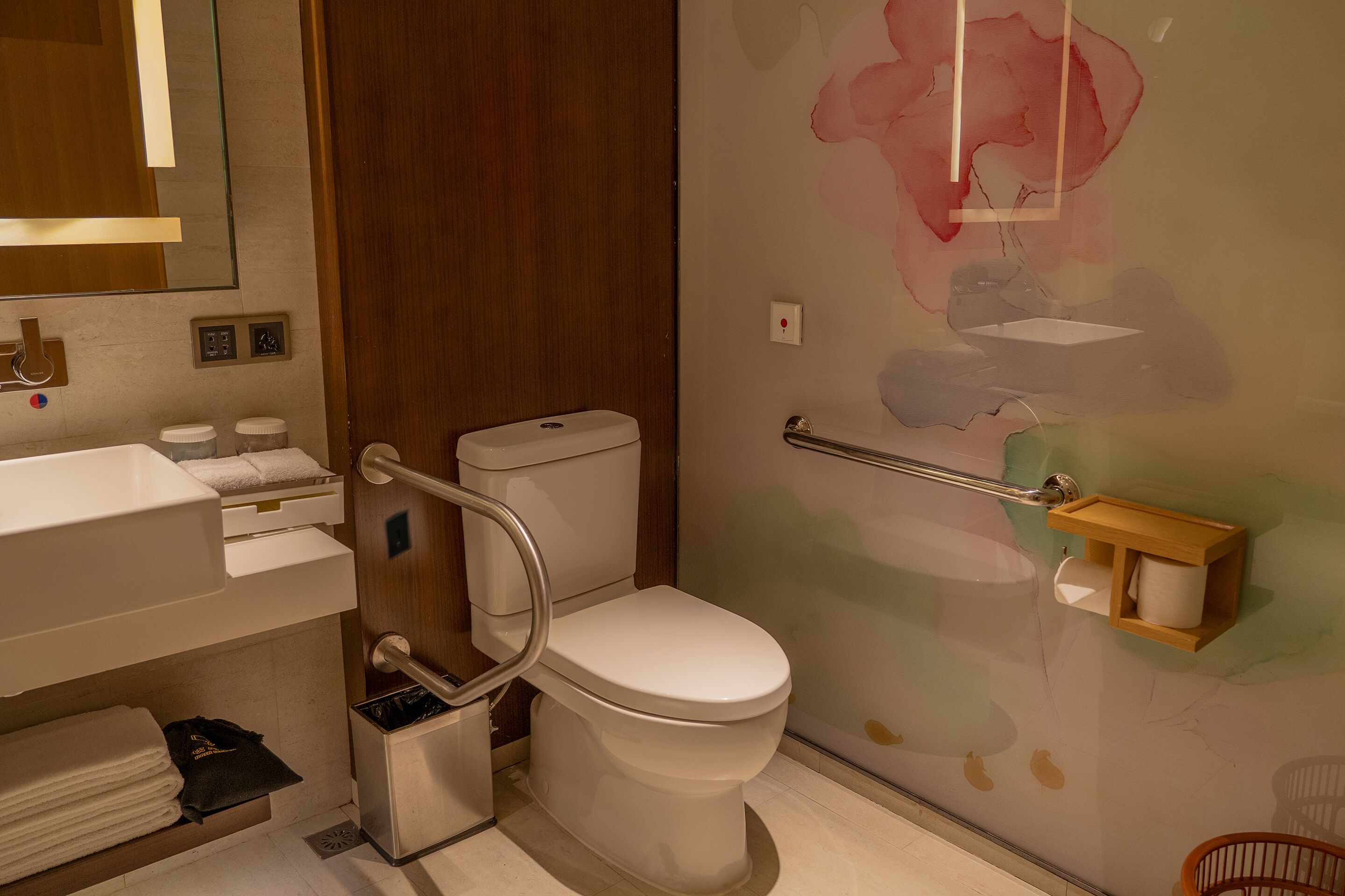 A modern bathroom with a white toilet, a sink with a mirror, and a wooden wall with a floral mural.