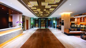 A modern hotel lobby with a wooden floor, a reception desk, a seating area, and a glass entrance. - Hilton Garden Inn Lijiang (Lijiang)