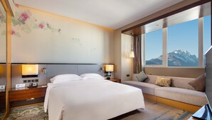 A hotel room with a bed, a sofa, a desk, and a large window offering a mountain view. - Hilton Garden Inn Lijiang (Lijiang)