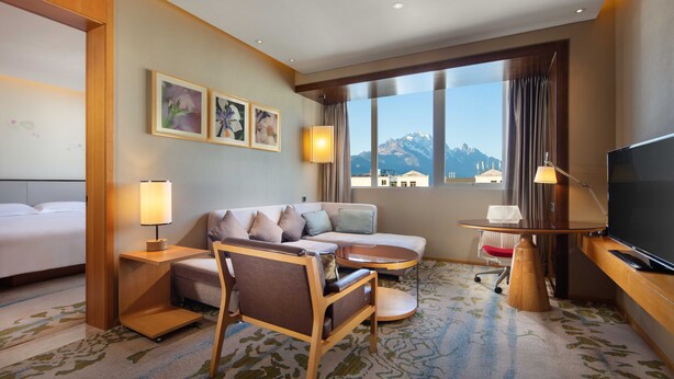 A hotel room with a sofa, armchair, TV, and a large window with a mountain view. - Hilton Garden Inn Lijiang (Lijiang)