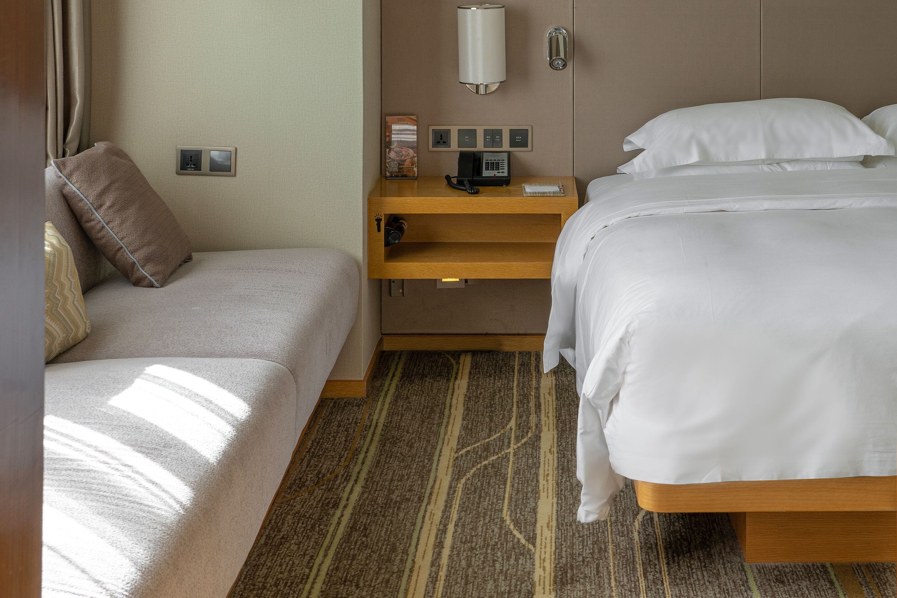 Habitación de hotel con cama, sofá, mesita de noche con teléfono y lámpara de pared.