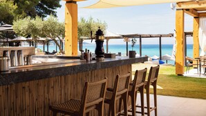 Un área de bar al aire libre con vistas al mar, pérgolas de madera y taburetes de mimbre.