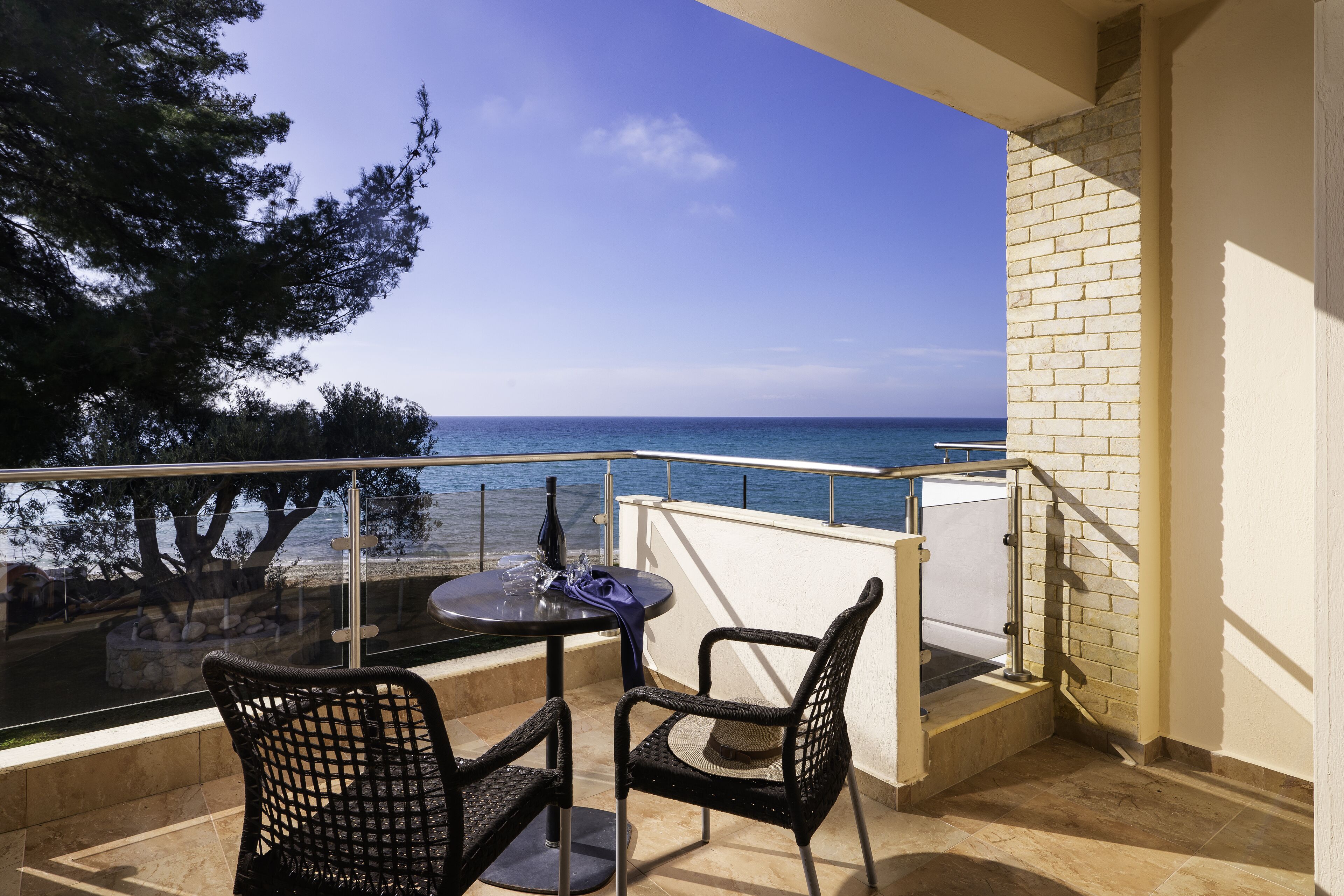 A balcony with a glass table and chairs, overlooking the sea.