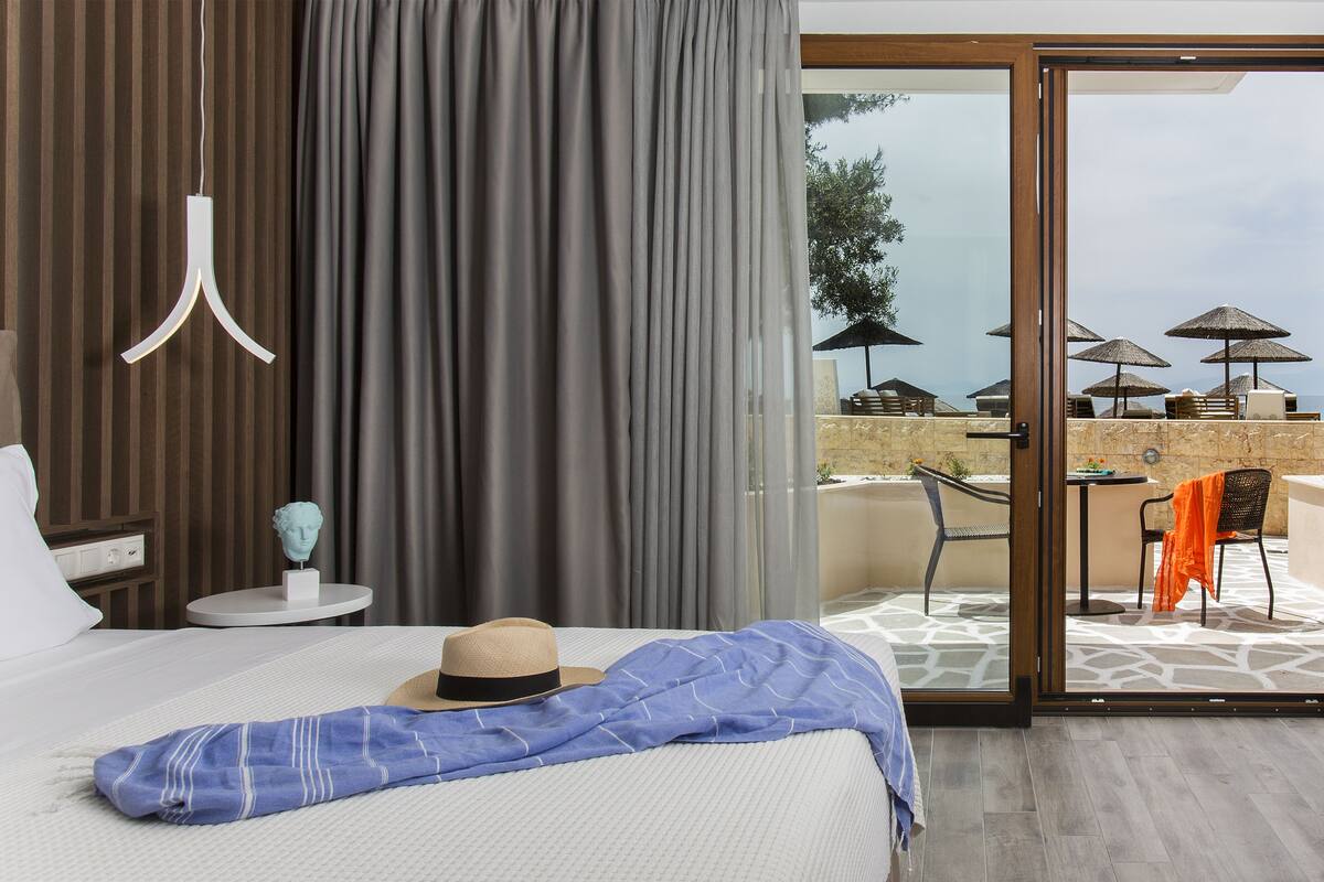 A hotel room with a bed, a small table with a bust sculpture, a hat, and a blue blanket.