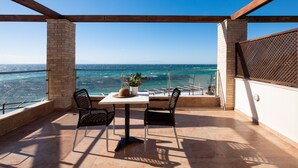 Un balcón con mesa y sillas, una planta en maceta y vista al mar.