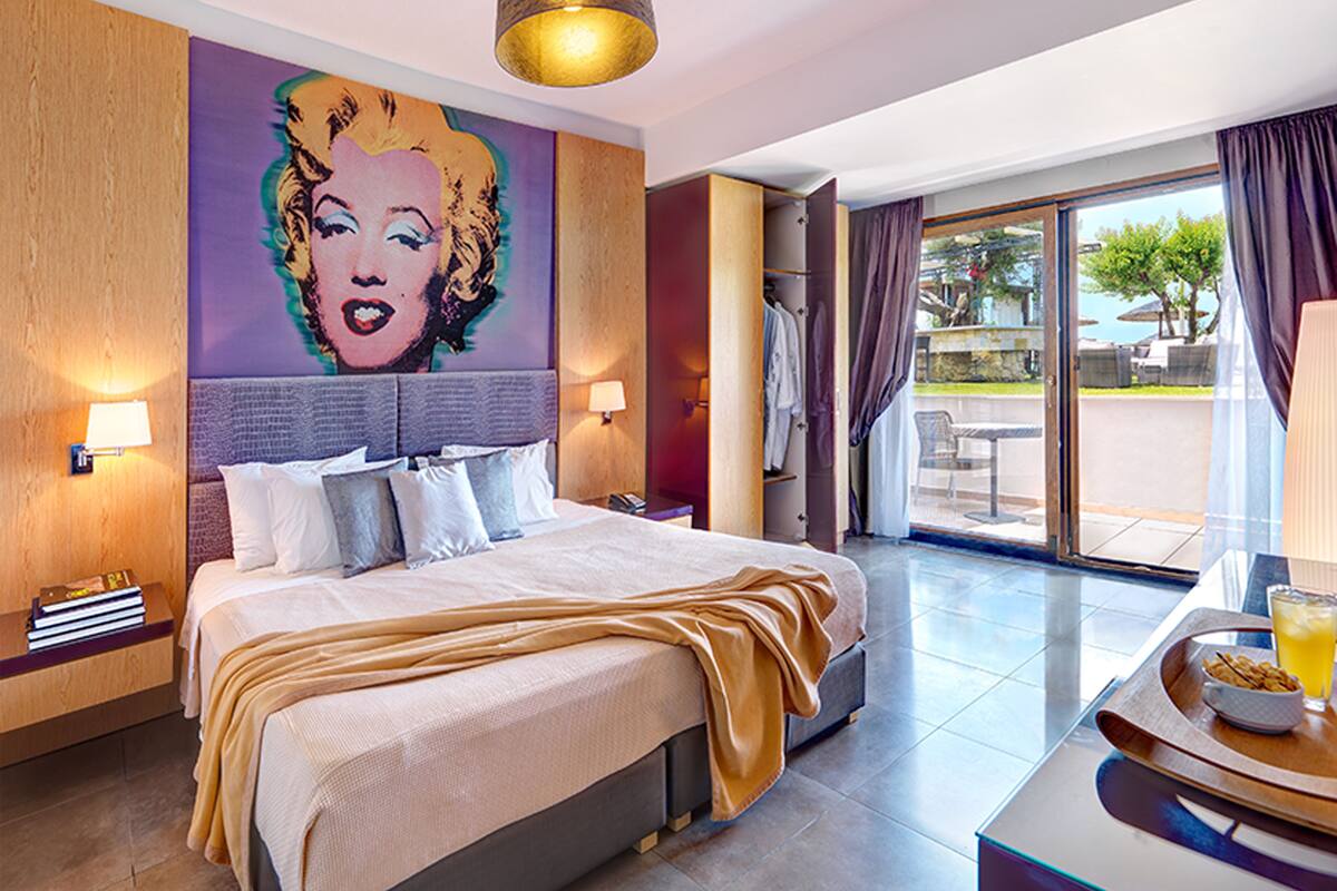 A hotel room with a large bed, a mural on the wall, a balcony with a view, and a breakfast tray on the side table.