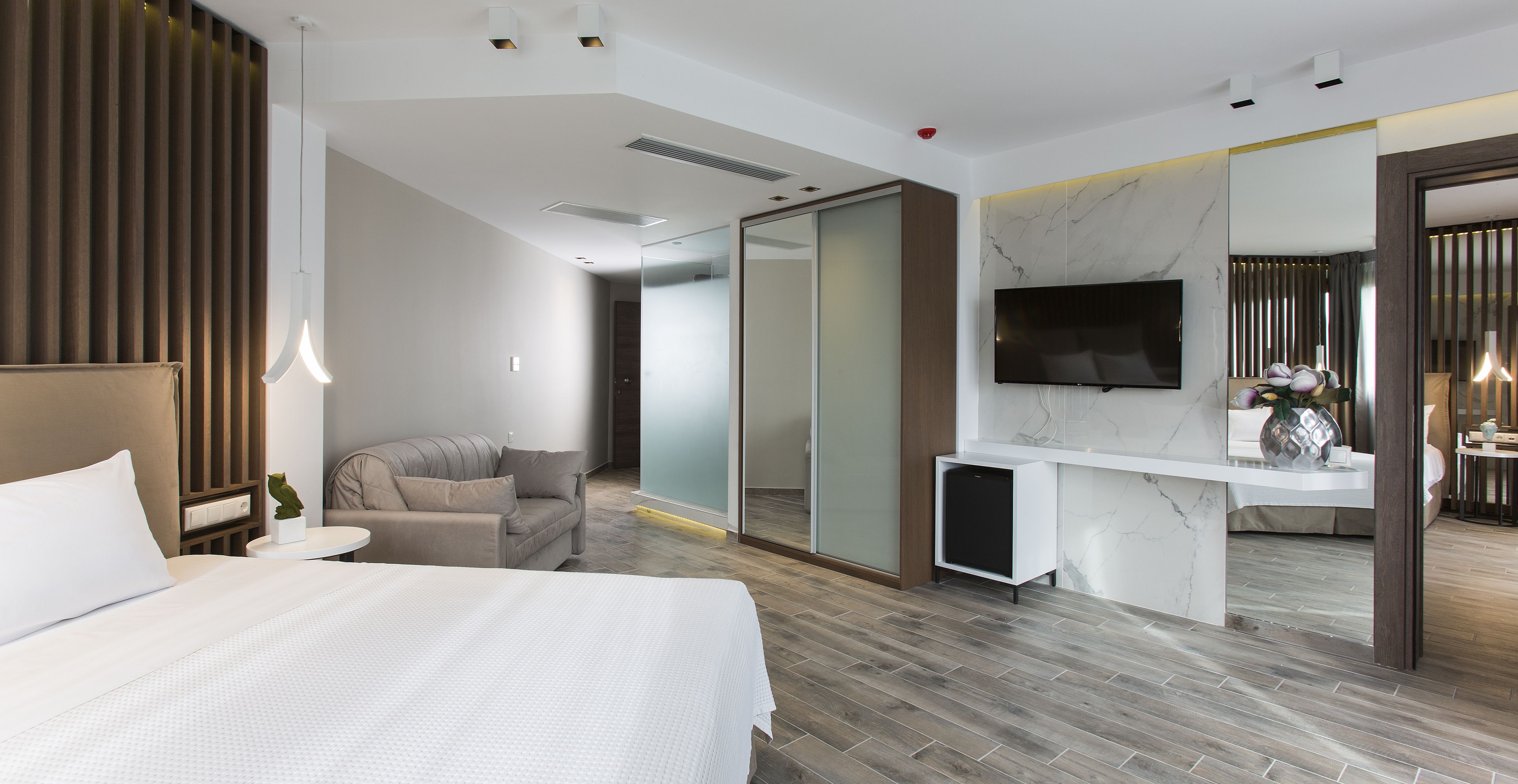 A modern hotel room with a large bed, a seating area, a desk, and a TV.