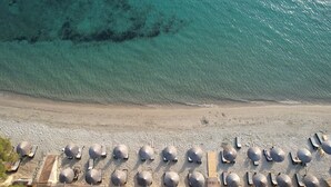 Vista aérea de una playa con filas de tumbonas y sombrillas, una orilla arenosa y agua turquesa cristalina.