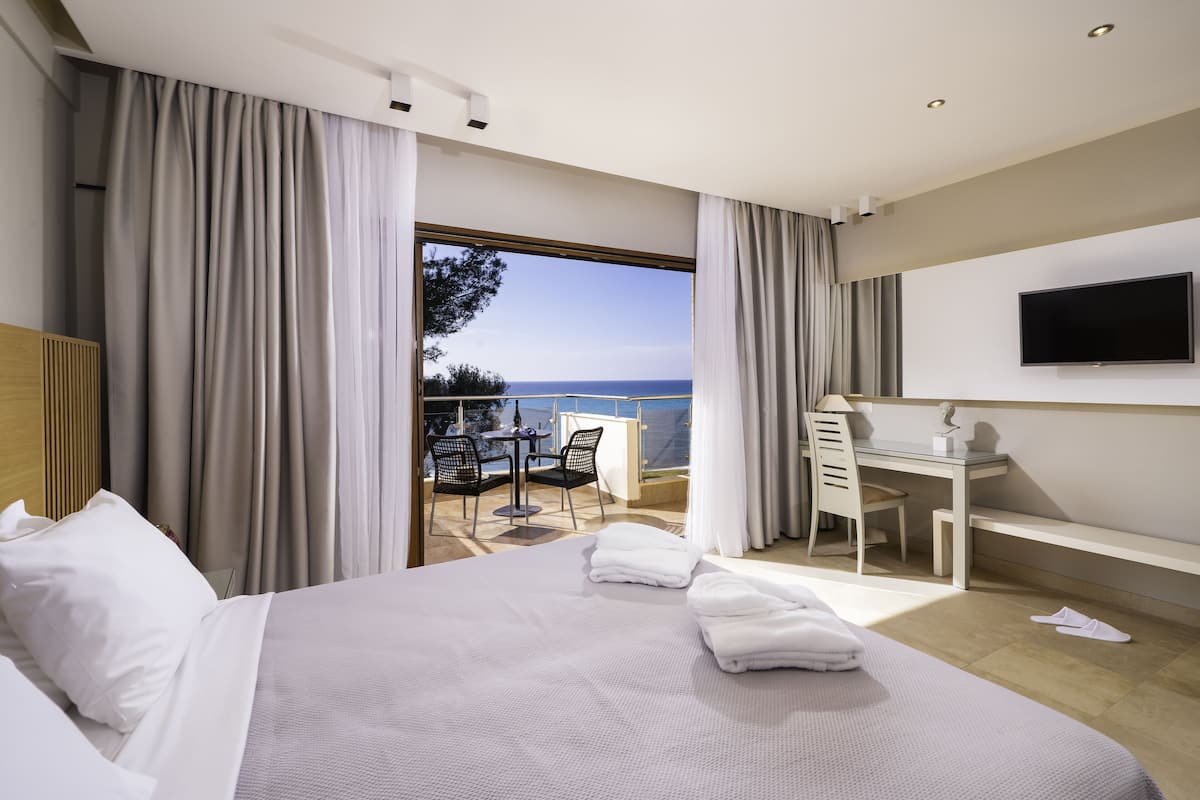 A hotel room with a large bed, a desk, and a view of the sea.