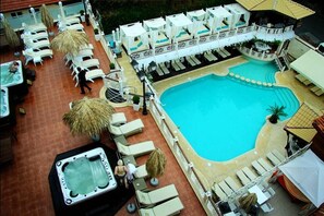 Un área de piscina en la azotea con sillones de descanso, un jacuzzi y una zona de estar cubierta.