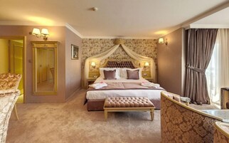 Habitación de hotel con una cama grande, un área de descanso, un espejo y una ventana con cortinas.