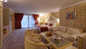 A hotel room with a bed, two sofas, a dining table, and a TV. - Spa Hotel Rich (Velingrad)