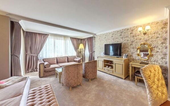 Habitación de hotel con sofá, sillón, televisión y un espejo decorativo.