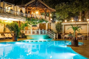 Un área de piscina con terraza cubierta, sillas de descanso y una escalera que lleva a un nivel superior.