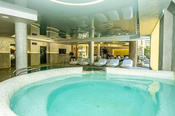 Área da piscina com espreguiçadeiras, teto de vidro e um balcão de recepção.
