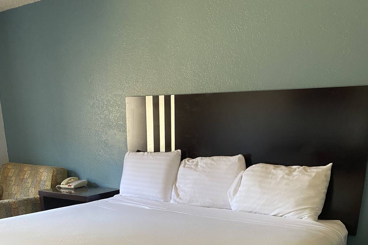 A large bed with white linens, a dark headboard, and a bedside table with a phone.