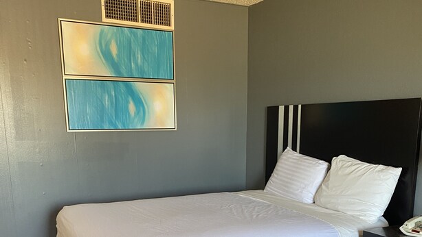 A hotel room with a bed, a bedside table, and a wall-mounted air vent. - Travel Inn Abilene (Abilene)