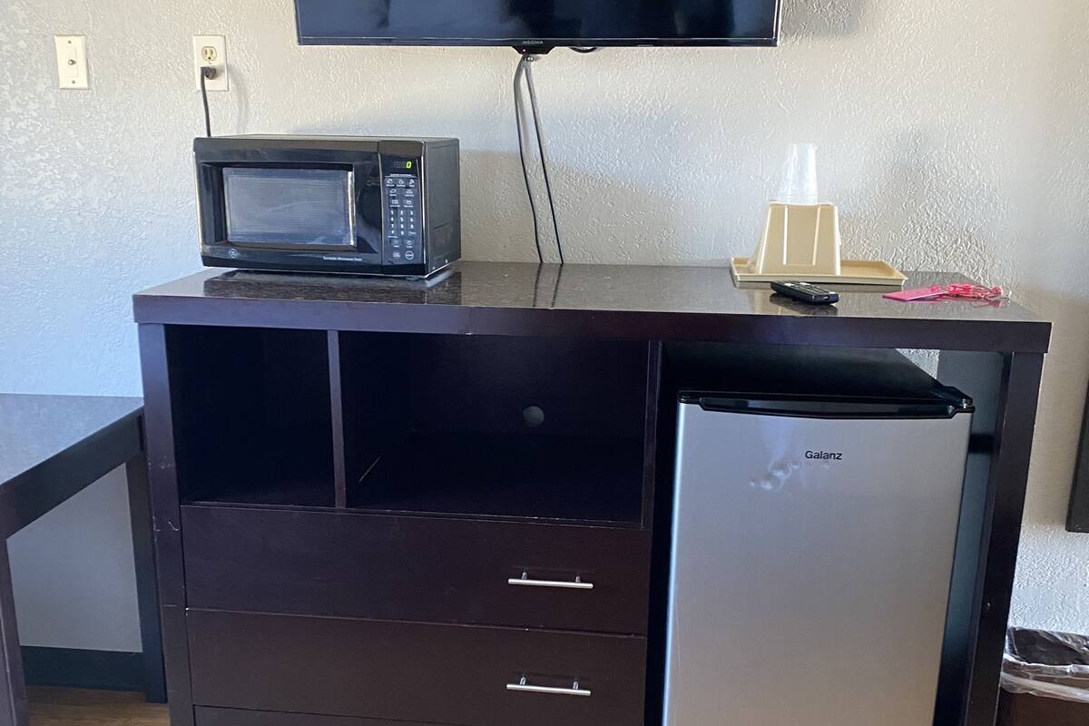 A compact kitchenette with a microwave, refrigerator, and a flat-screen TV mounted on the wall.