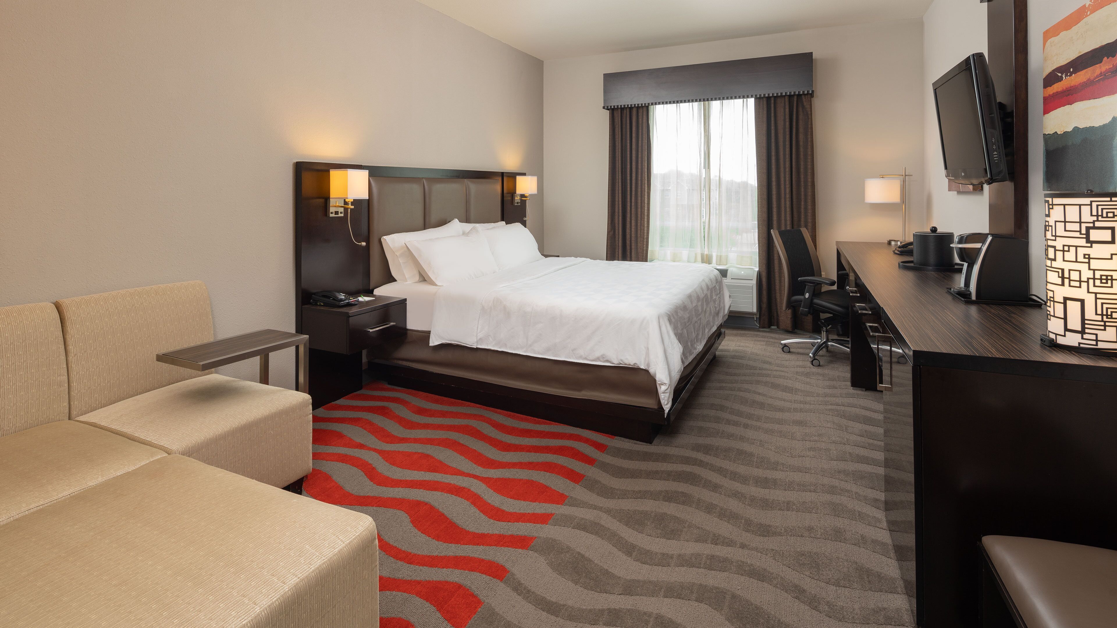 A hotel room with a bed, a desk, a TV, a chair, and a sofa.