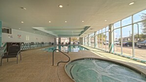 Une piscine intérieure à l’eau claire, entourée de chaises longues et dotée d’une grande fenêtre donnant sur l’extérieur.