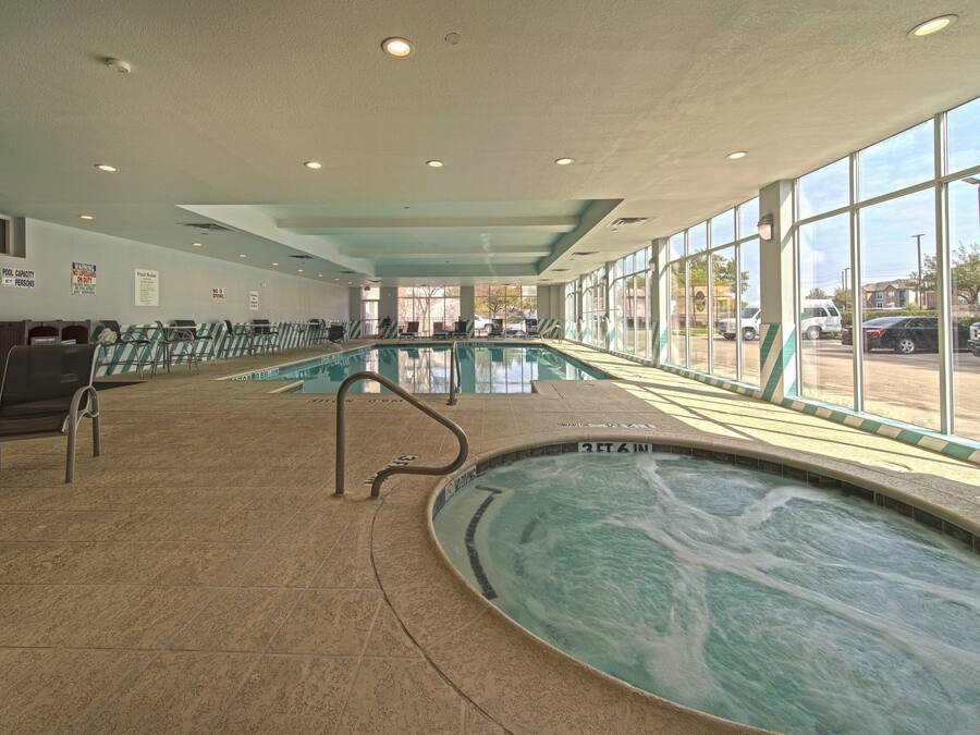 Piscina interna com água cristalina, cercada por espreguiçadeiras e uma grande janela com vista para o exterior.