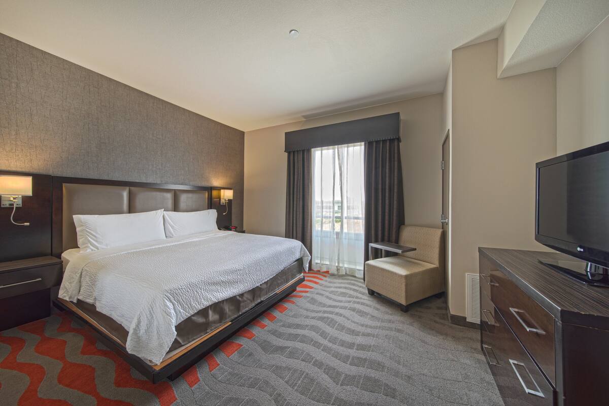 A hotel room with a large bed, a TV, a chair, and a desk.