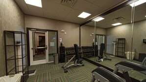 Une salle de sport équipée de matériel d’exercice, d’un miroir et d’une porte donnant sur un vestiaire.