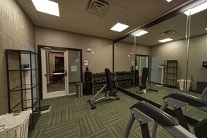 Ein Fitnessraum mit Trainingsgeräten, einem Spiegel und einer Tür zu Umkleideräumen.