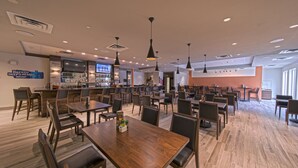 En rymlig restaurang med många bord och stolar, en bardisk och en tv-skärm.