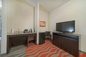 Ein kleines Hotelzimmer mit Küchenzeile, Flachbildfernseher und Mikrowelle.