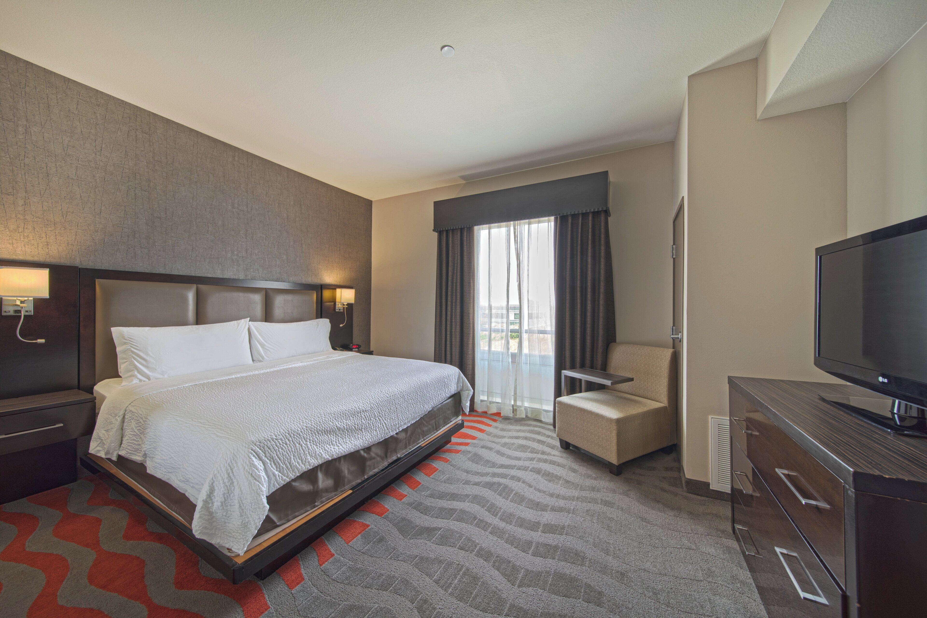 A hotel room with a large bed, a TV, a chair, and a desk.