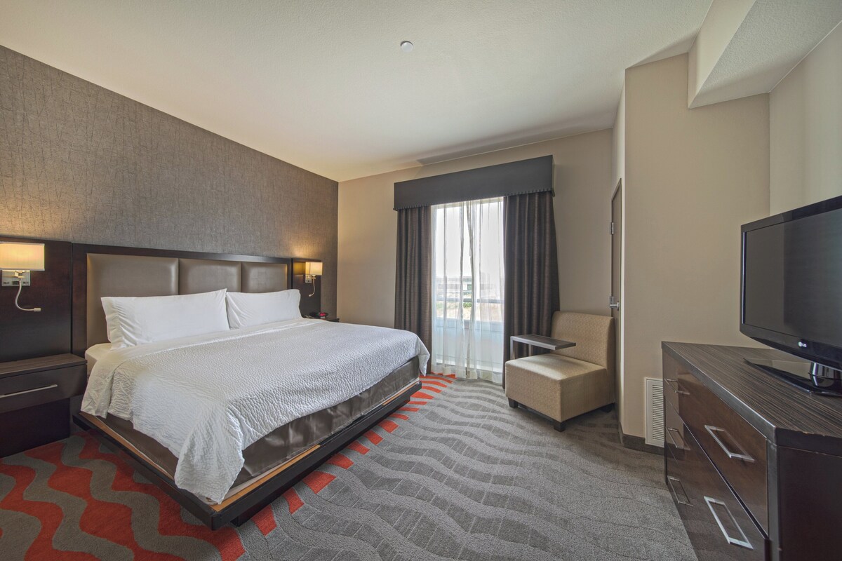 Ein Hotelzimmer mit einem großen Bett, einem Fernseher, einem Sessel und einem Schreibtisch.