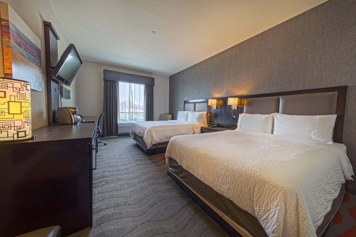 A hotel room with two beds, a desk with a chair, a television, and a window with curtains.