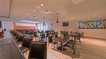 A spacious restaurant with multiple tables and chairs, a long counter, and a large mural on the wall.