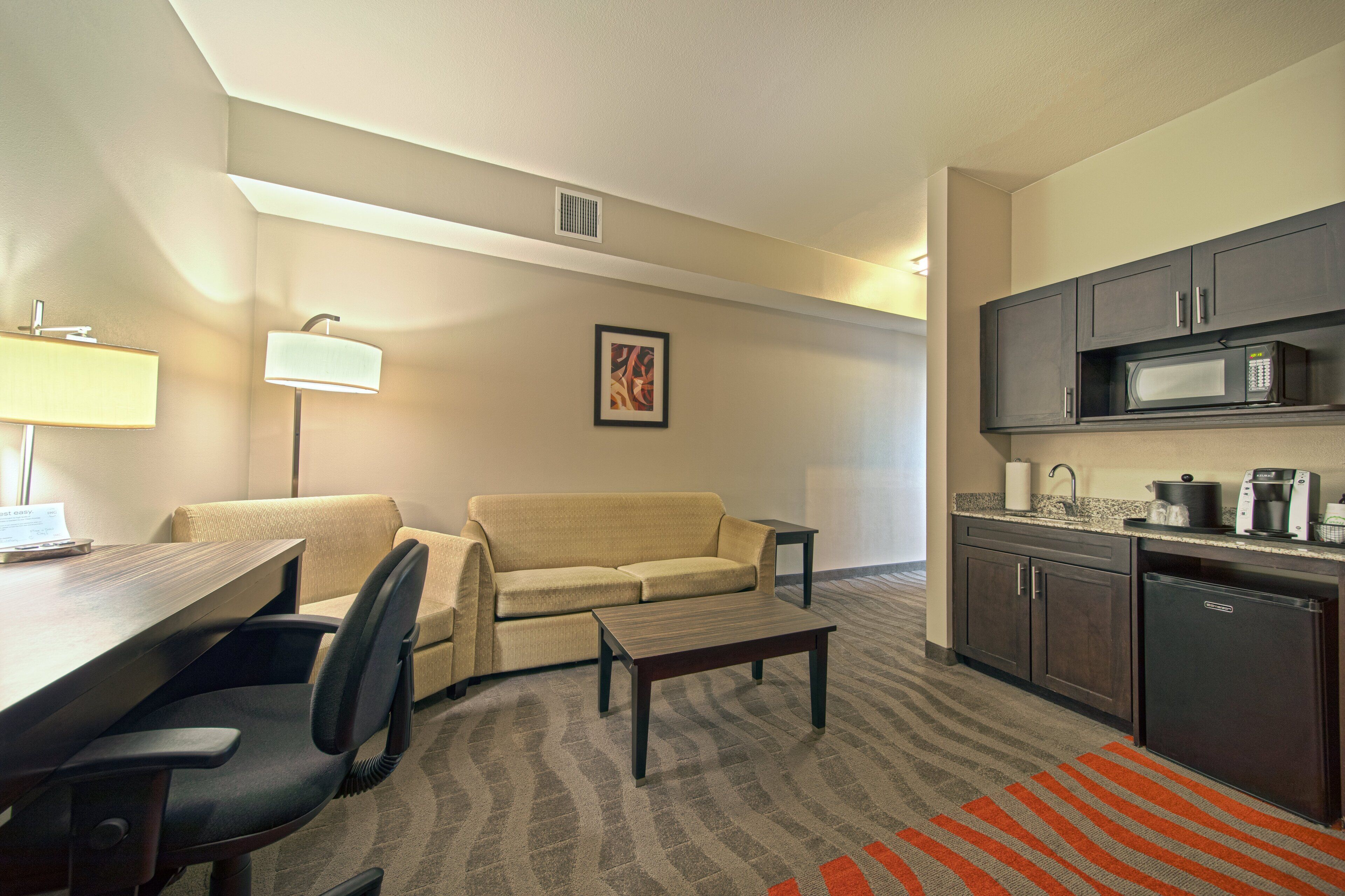 A hotel room with a kitchenette, a sofa, a dining table, and a chair.