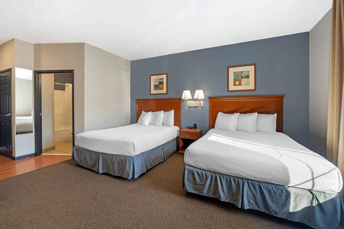 A hotel room with two beds, a bathroom, and a door leading to another room.
