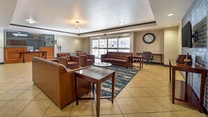 Un hall d’entrée spacieux, doté de canapés en cuir, d’une table basse, d’un comptoir de réception et d’une grande fenêtre avec une horloge.