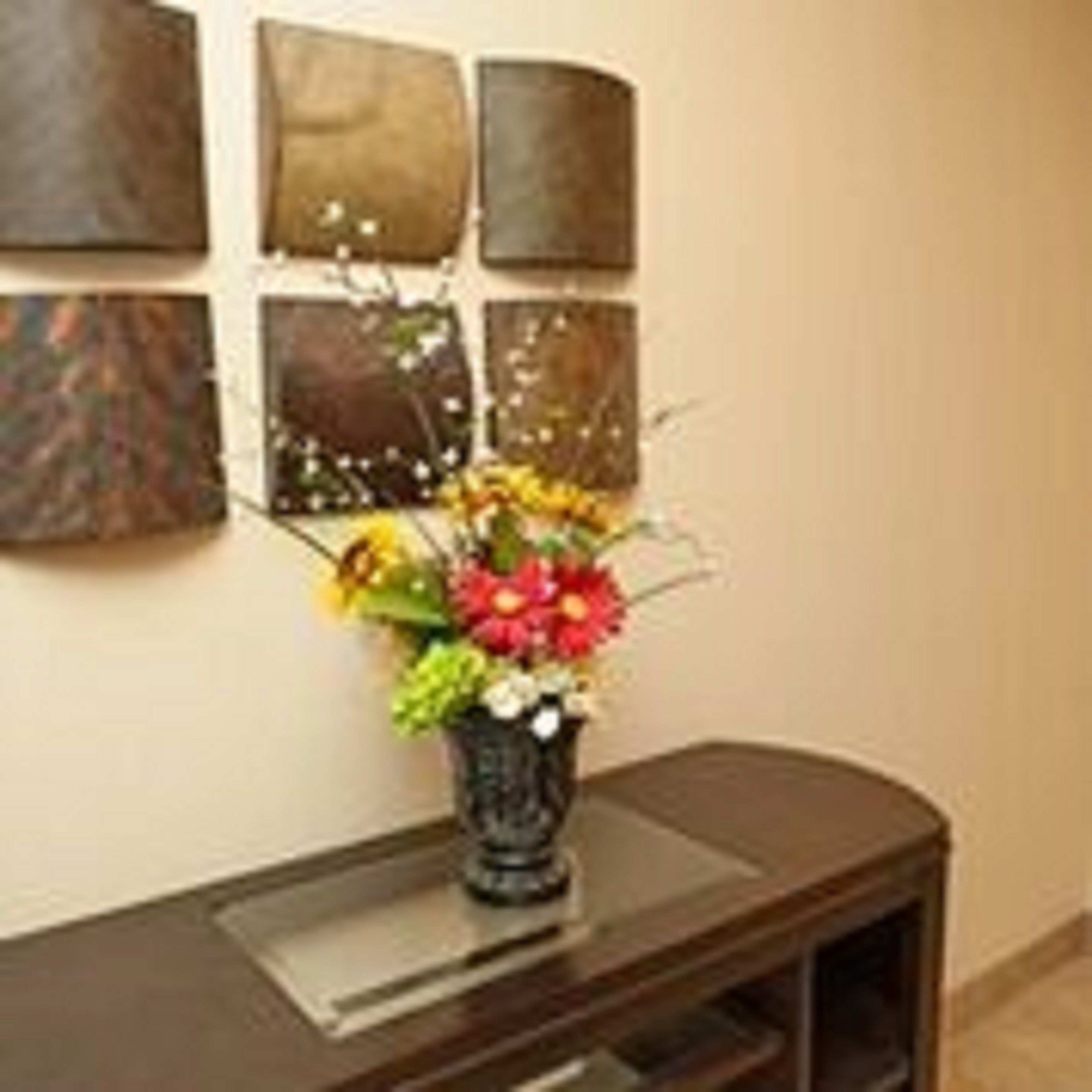 Un mur orné de six œuvres d’art de forme carrée et un vase rempli de fleurs, posé sur une console en bois foncé.