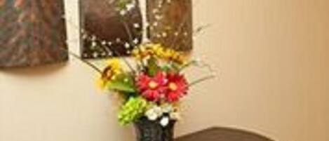 Un mur orné de six œuvres d’art de forme carrée et un vase rempli de fleurs, posé sur une console en bois foncé.