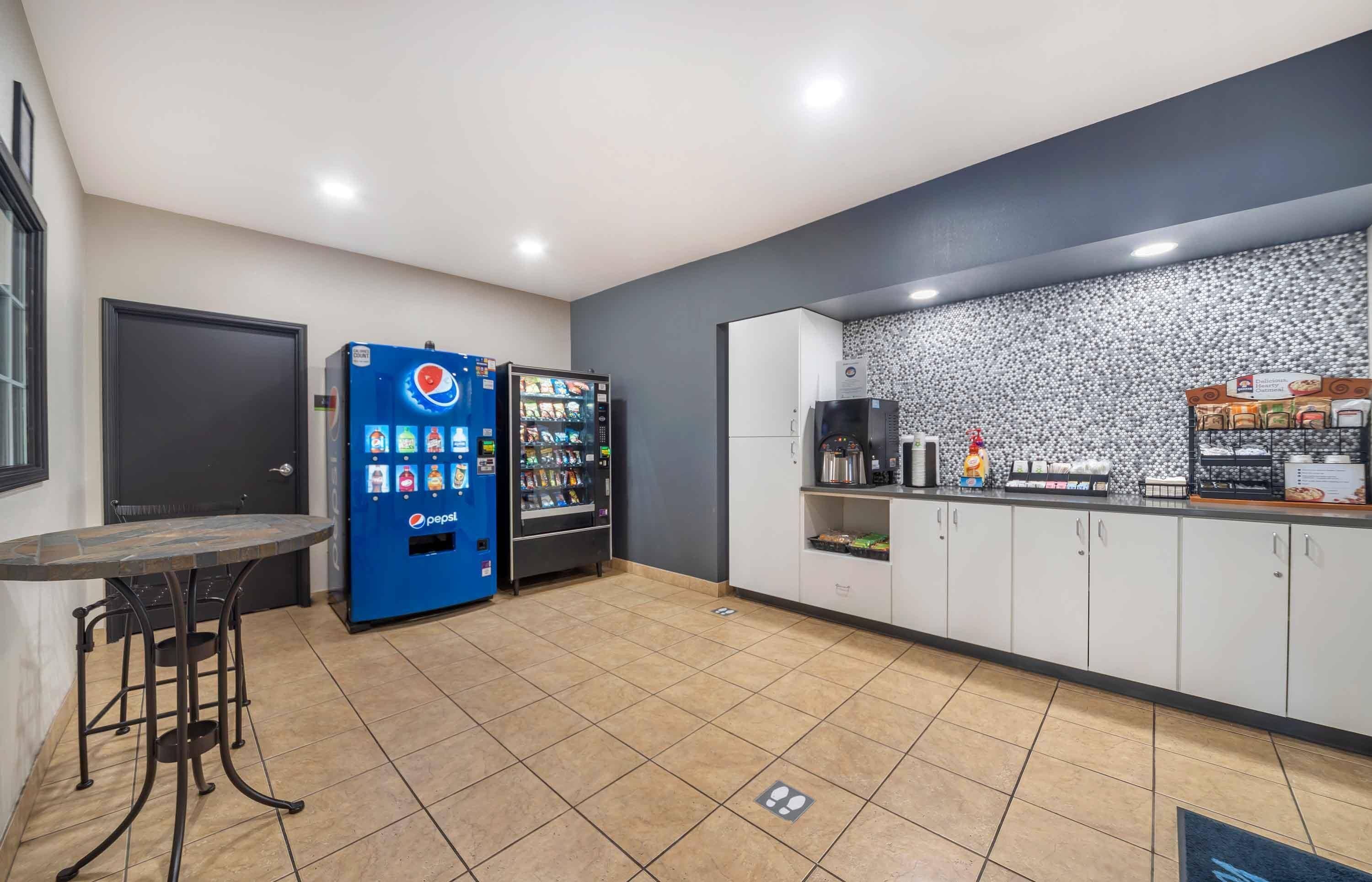 A modern kitchen area with a coffee machine, a refrigerator, and a vending machine.