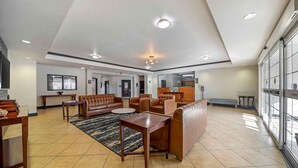 Un hall d’entrée spacieux avec un plafond haut, des luminaires encastrés, un ensemble de canapés en cuir, une table basse et un tapis à motifs.