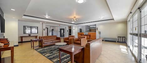 A spacious lobby with a high ceiling, recessed lighting, a leather sofa set, a coffee table, and a patterned rug.