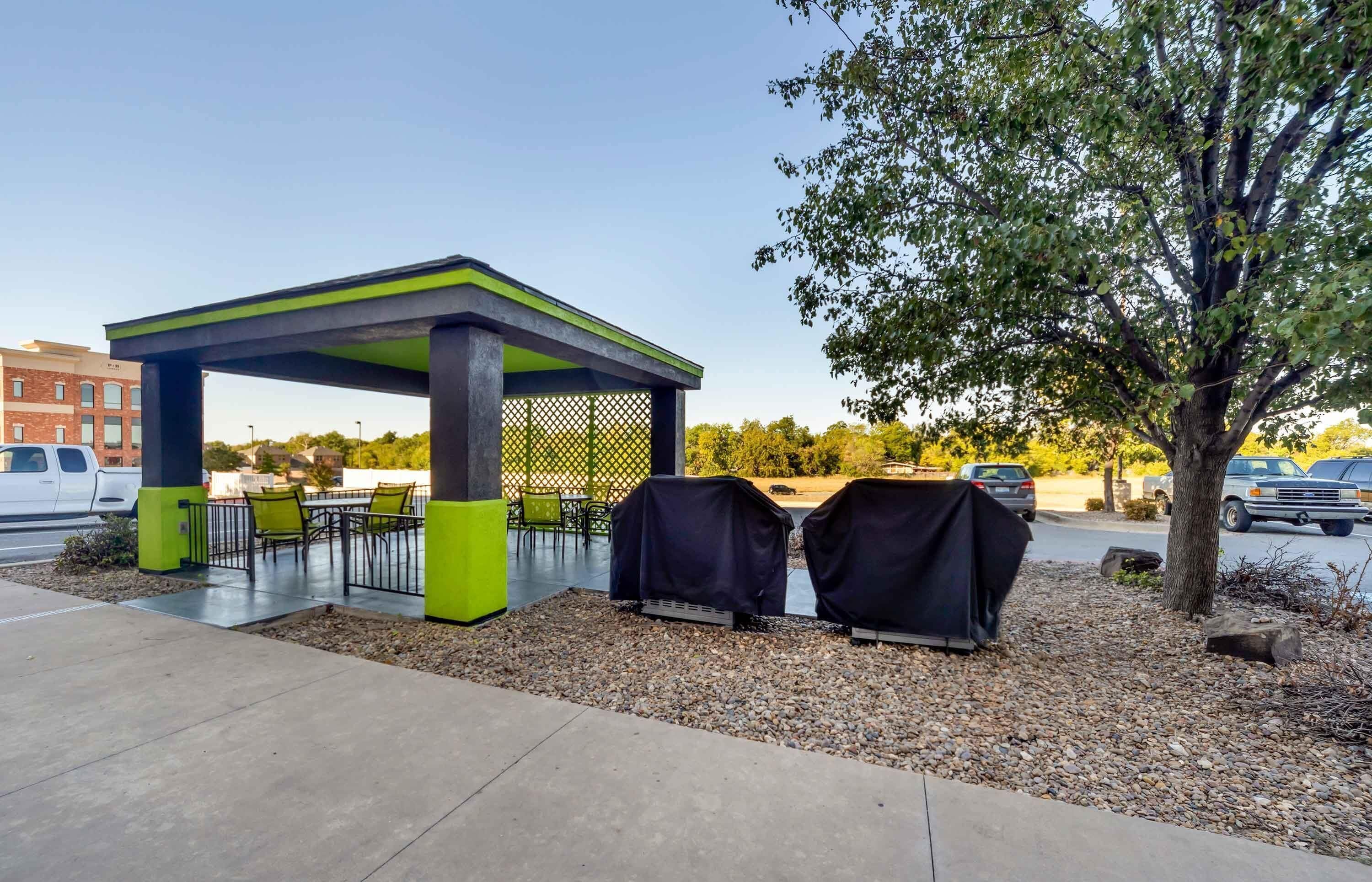 A covered outdoor seating area with tables and chairs, a grill, and a tree.