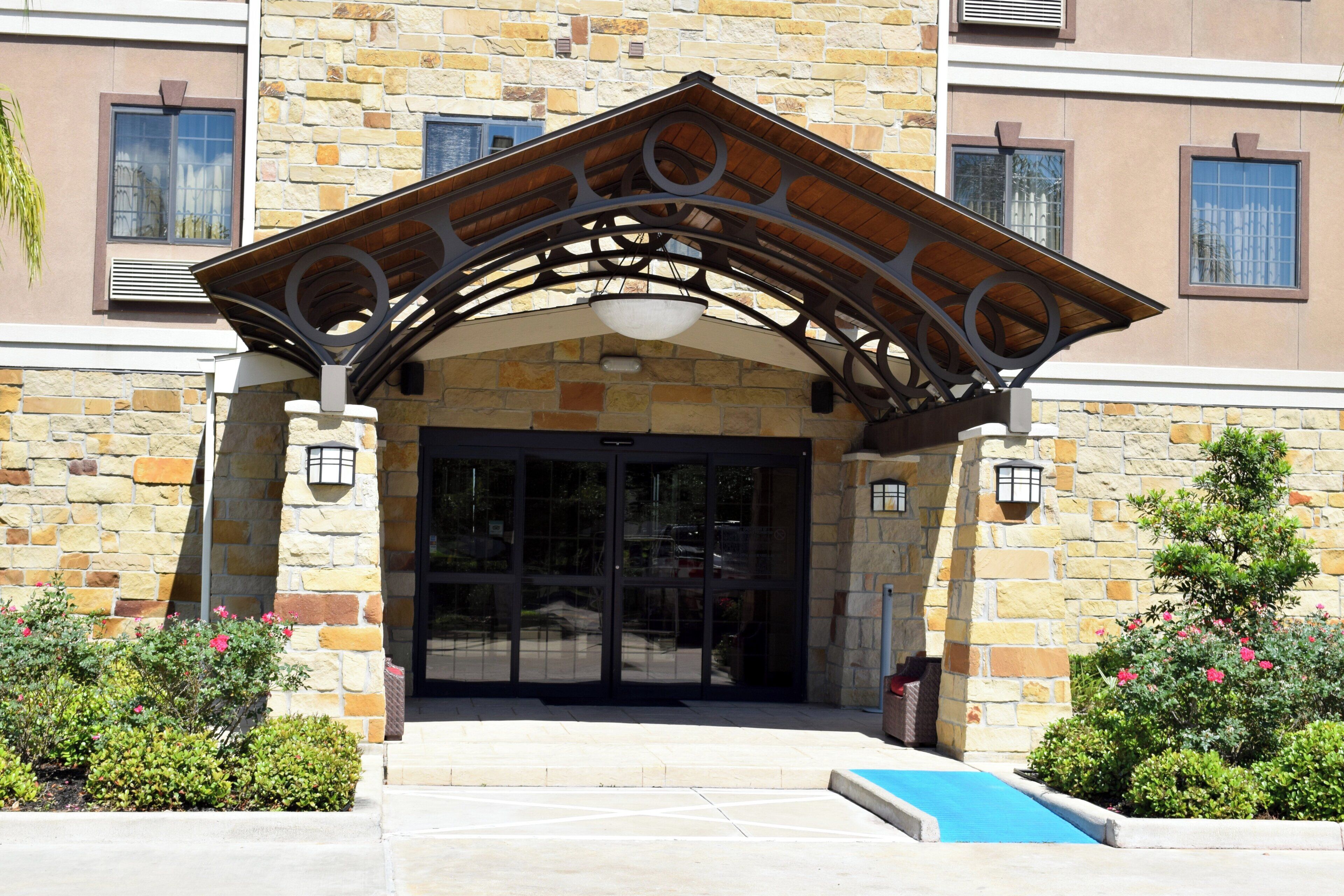 A stone building with a wooden entrance canopy, glass doors, and a small pool area.